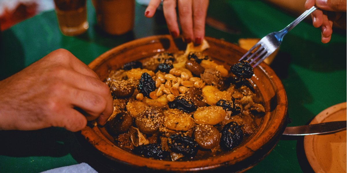 Hands sharing a Moroccan tagine with dried fruit and nuts at the table