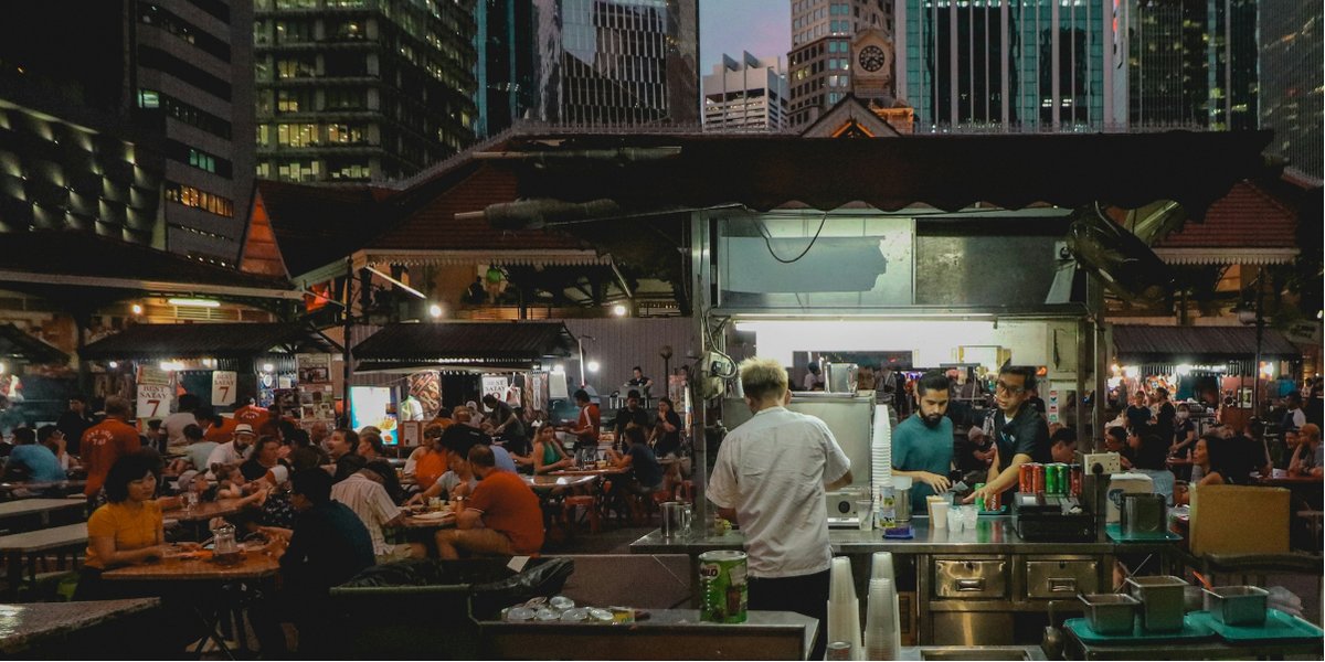 Hawker food stall at night with the Singapore skyline in the background
