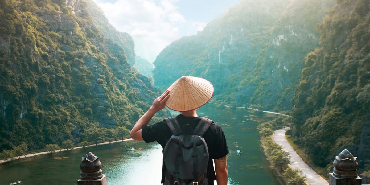 A solo traveller in a conical hat looking out over a river valley in Vietnam